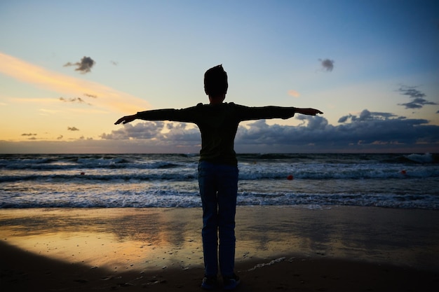 Silhouette d'enfant debout sur la plage de la mer et regardant les vagues