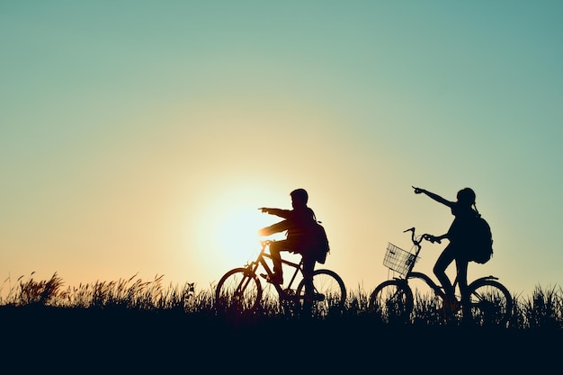 Silhouette d'enfants avec un vélo contre un ciel dégagé