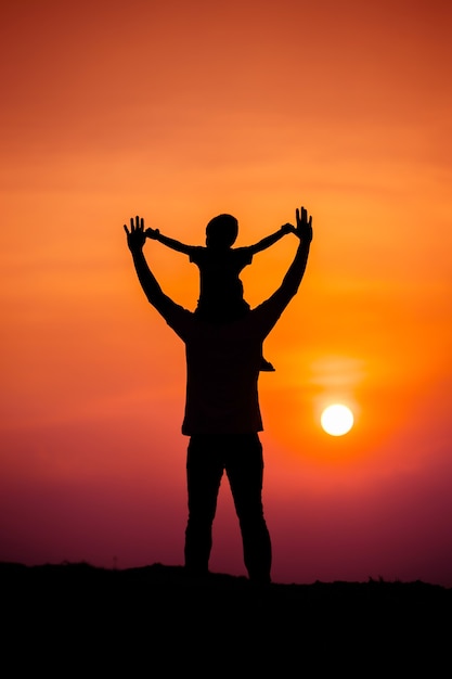 Silhouette d'une famille avec un garçon chevauchant joyeusement le cou de son père contre le ciel au coucher du soleil