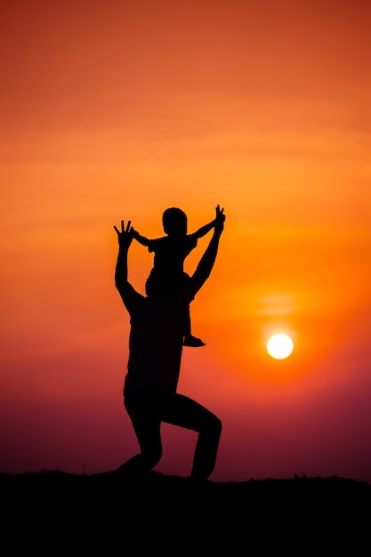 Silhouette d'une famille avec un garçon chevauchant joyeusement le cou de son père contre le ciel au coucher du soleil