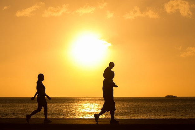 Silhouette de famille marchant sur la plage avec bébé sur le cou