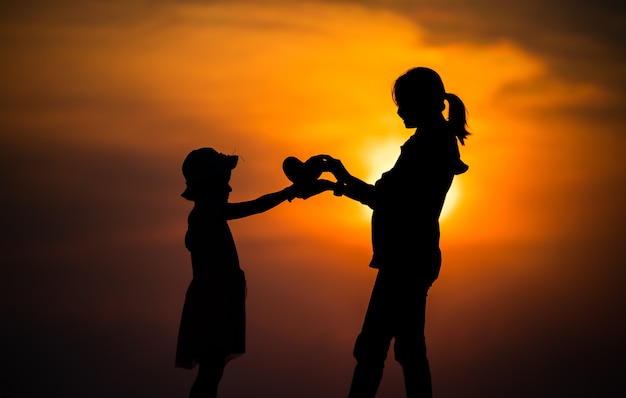 Silhouette d'une famille avec une mère heureuse jouant avec une fille dans le ciel coucher de soleil