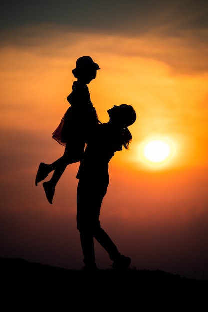 Silhouette d'une famille avec une mère heureuse jouant avec une fille dans le ciel coucher de soleil