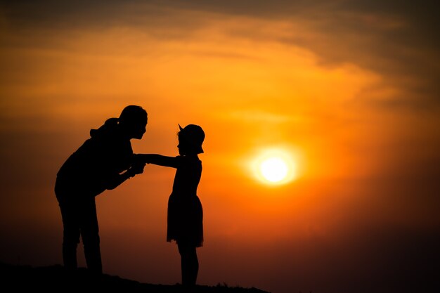 Silhouette d'une famille avec une mère heureuse jouant avec une fille dans le ciel coucher de soleil