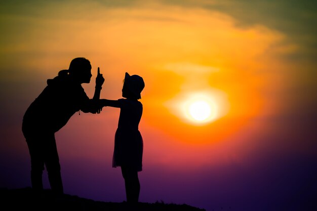 Silhouette d'une famille avec une mère heureuse jouant avec une fille dans le ciel coucher de soleil