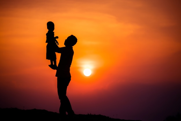 Silhouette de la famille que le père joue avec le garçon joyeusement avec le ciel coucher de soleil