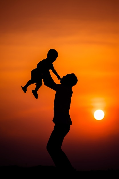 Silhouette de la famille que le père joue avec le garçon joyeusement avec le ciel coucher de soleil