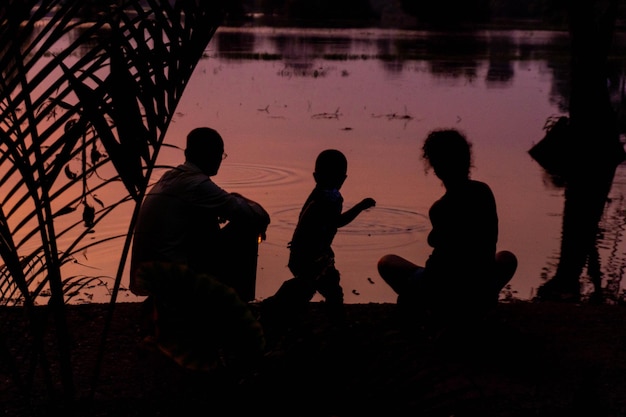 Silhouette de famille sur la rive du fleuve au coucher du soleil