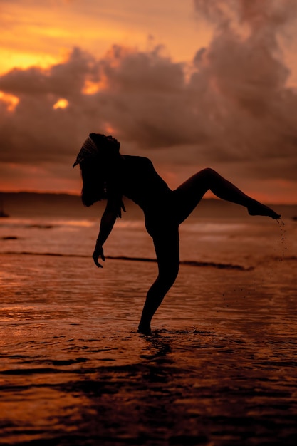 Silhouette d'une femme asiatique jouant dans l'eau sur la plage avec de fortes vagues se brisant