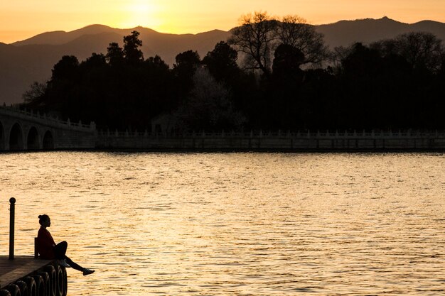 Silhouette d'une femme assise sur une jetée au coucher du soleil, Pékin, Chine