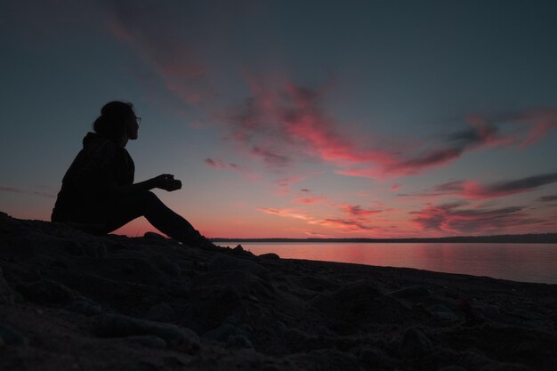 La silhouette d'une femme assise sur la plage Elle admire le ciel au coucher du soleil