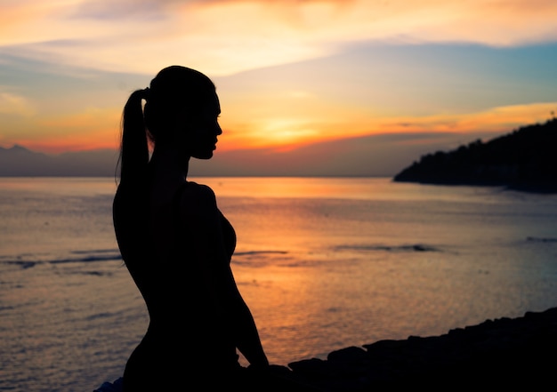 Silhouette d'une femme assise sur une plage avec le message inspirant de Croyez en votre potentiel contre une surface de coucher de soleil