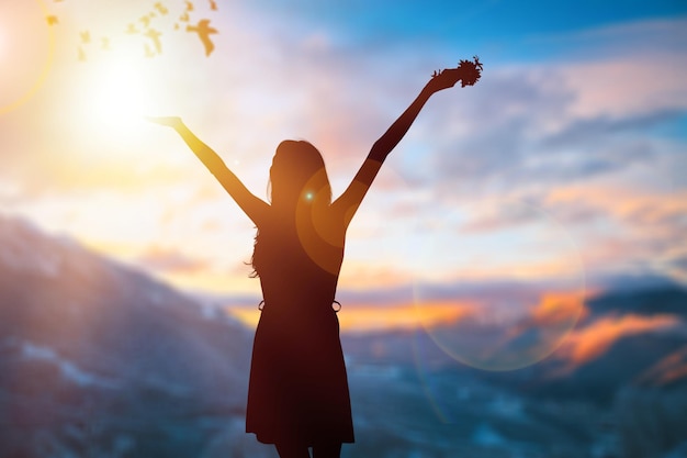 Silhouette de femme en bonne santé a levé les mains au pré sur fond de coucher de soleil