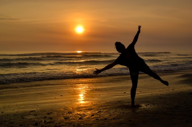 Silhouette d'une femme à bras ouverts sur le rivage d'une plage au coucher du soleil L'heure d'or