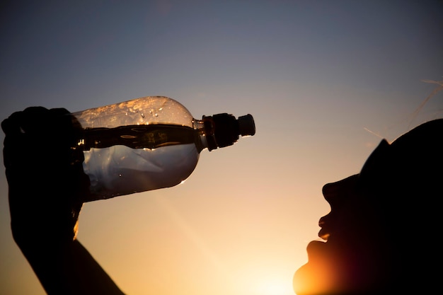 Silhouette d'une femme buvant de l'eau au coucher du soleil