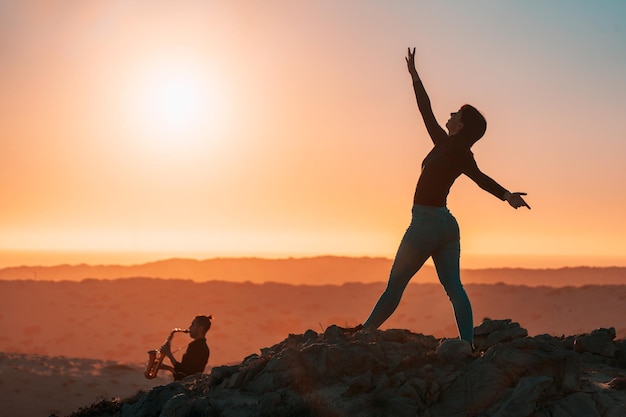 Silhouette de femme dansant au rythme de la musique de saxophone dans le désert au coucher du soleil