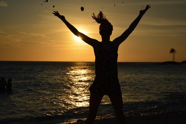 Photo silhouette d'une femme debout au bord de la mer contre le ciel au coucher du soleil