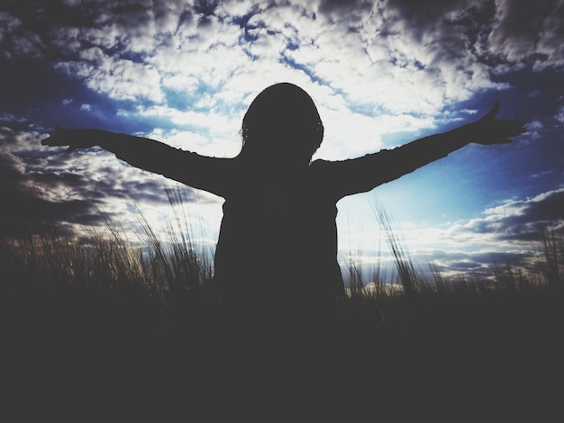 Photo silhouette d'une femme debout avec les bras tendus dans le champ