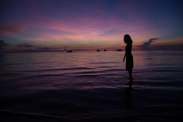 Silhouette d'une femme debout sur le rivage contre le ciel au coucher du soleil