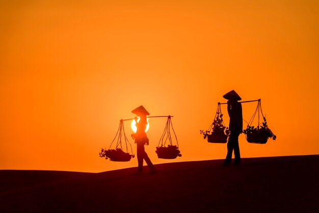 silhouette femme, sur, dune sable, à, coucher soleil, porter, paniers