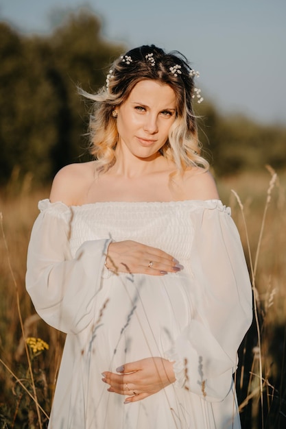 Silhouette d'une femme enceinte en robe blanche au coucher du soleil