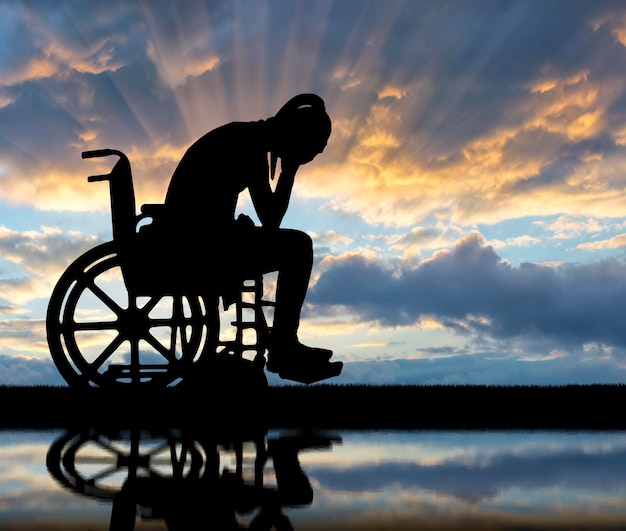 Silhouette d'une femme handicapée triste dans un fauteuil roulant au bord de la rivière avec son reflet. Le concept des personnes handicapées éprouvant du chagrin et de la tristesse