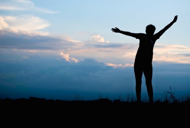 Silhouette de femme heureuse sautant dans le champ vert contre le ciel bleu.