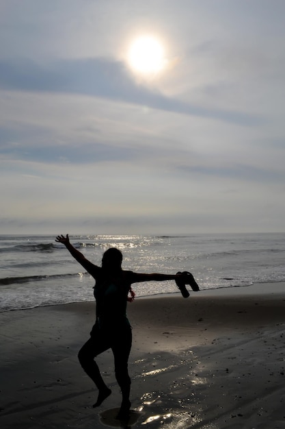 Silhouette de femme heureuse sautant sur le rivage d'une plage au coucher du soleil