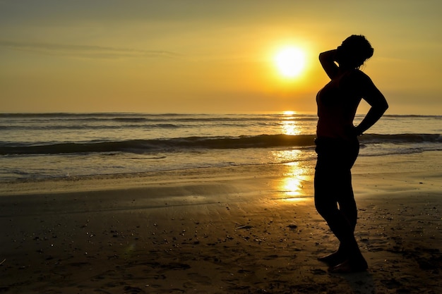 Silhouette d'une femme posant sensuellement sur le rivage d'une plage au coucher du soleil L'heure d'or