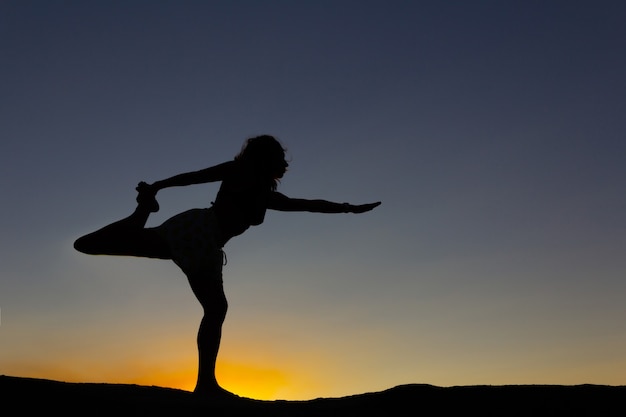 Photo silhouette de femme pratiquant le yoga au coucher du soleil sur un rocher dans la nature. rétro-éclairage. espace de copie.