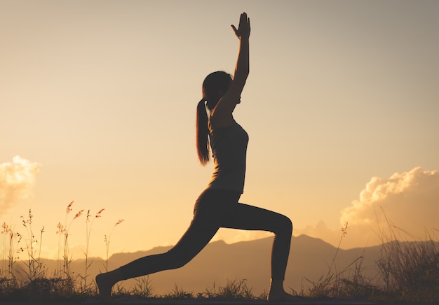 Silhouette femme pratiquant le yoga au sommet de la montagne