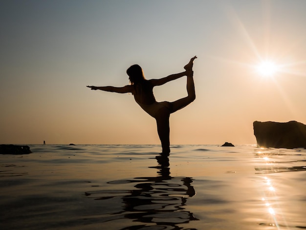 Silhouette d'une femme pratiquant le yoga en mer au coucher du soleil