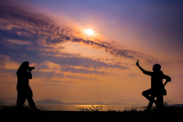 La silhouette d'une femme à prendre des photos dans le contexte du lever du soleil à la belle vue sur la montagne du réservoir.