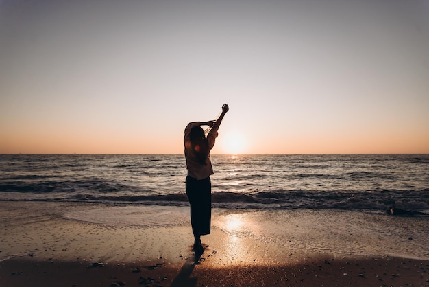 Silhouette d'une femme regardant le coucher du soleil sur la plage