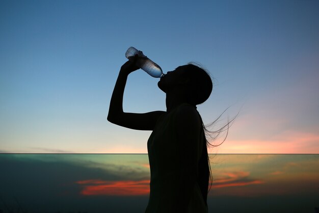 Silhouette de femme Réhydrater et rafraîchir au coucher du soleil sur le toit de l&#39;immeuble