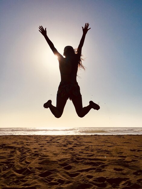 Photo la silhouette d'une femme sautant sur le sable contre le ciel