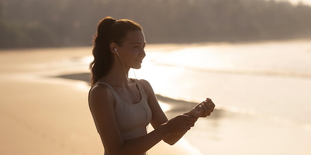 Silhouette d'une femme sportive en bonne santé dans des vêtements de fitness mesure le pouls à la main sur la plage au mor