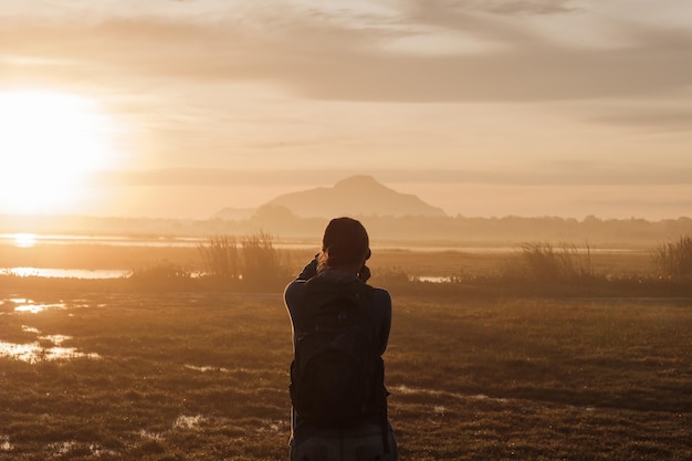 Silhouette d'une femme tenant un smartphone prenant des photos à l'extérieur pendant le lever ou le coucher du soleil