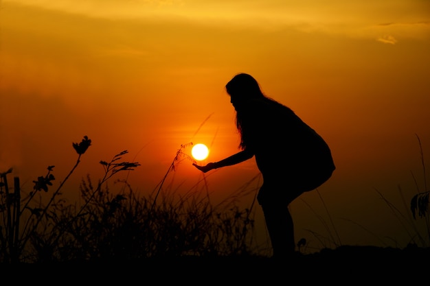 La silhouette d&#39;une femme tenant le soleil a un fond de coucher de soleil