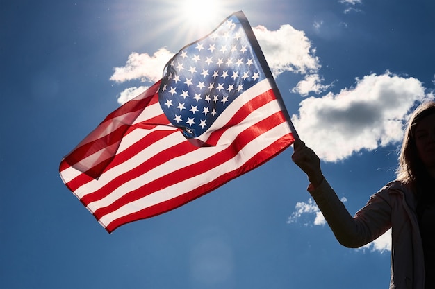 La silhouette de femme tient le drapeau national des Etats-Unis contre le ciel nuageux bleu