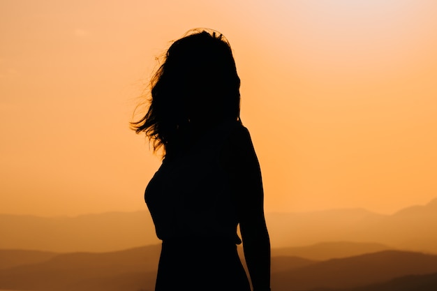 Silhouette de femmes au coucher du soleil orange sur une falaise surplombant les montagnes