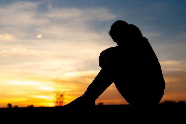 Silhouette de femmes tristes et déprimées assises à l'allée du parc avec coucher de soleil