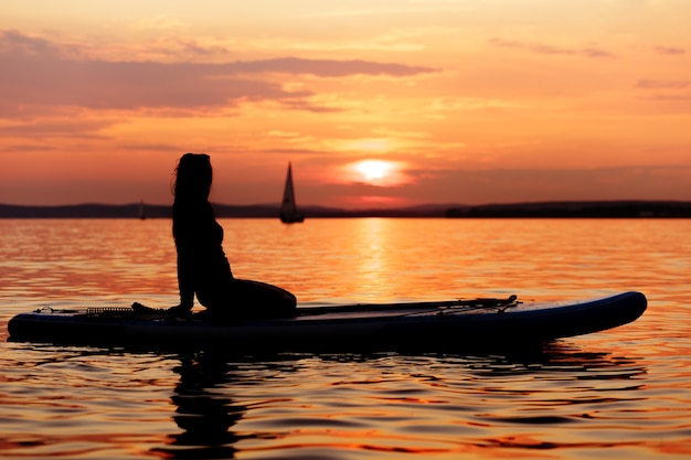 Silhouette d'une fille assise sur une planche de paddle au coucher du soleil