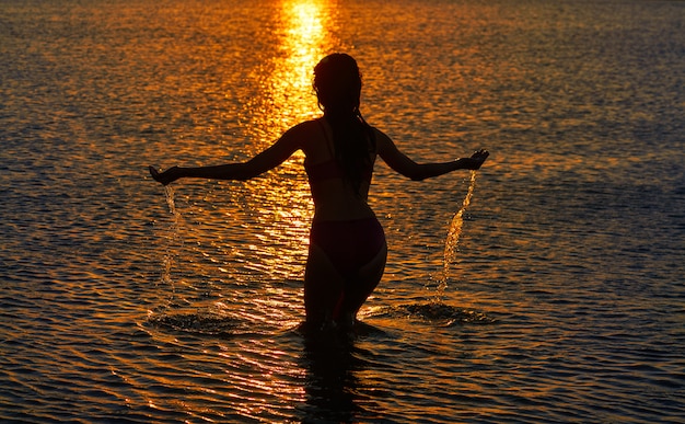 Silhouette de fille au coucher du soleil à la plage, bras ouverts