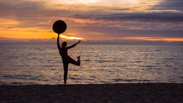 Silhouette d'une fille avec un chapeau à la main au bord de la mer au coucher du soleil.