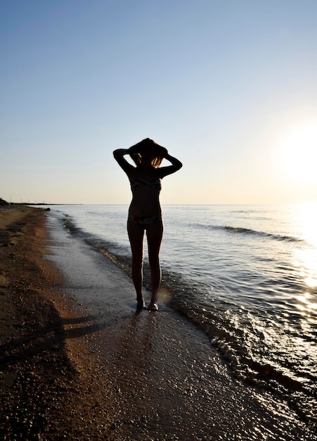 Silhouette d'une fille contre le coucher de soleil au bord de la mer La silhouette sombre contre le couché de soleil de la mer Fille sur la plage le soir