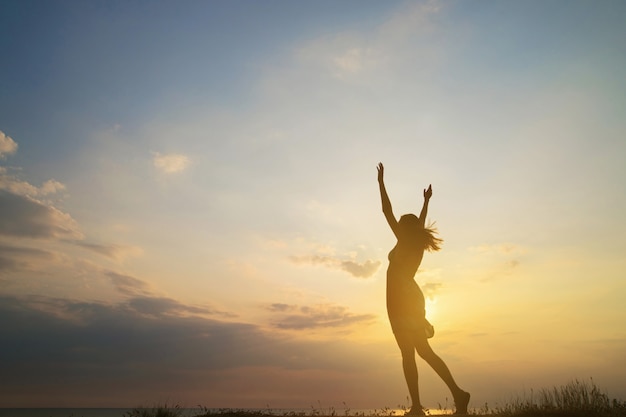 Silhouette fille heureuse en robe d'été debout sur la plage dans le contexte d'un beau coucher de soleil