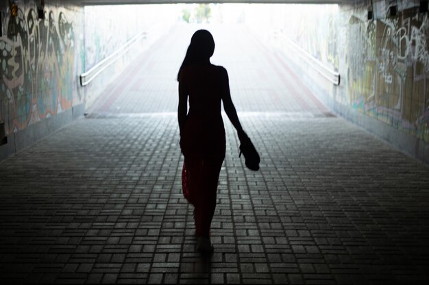 Silhouette d'une fille en robe longue allant à la sortie d'un passage pour piétons souterrain. Mise au point douce. Résumé.