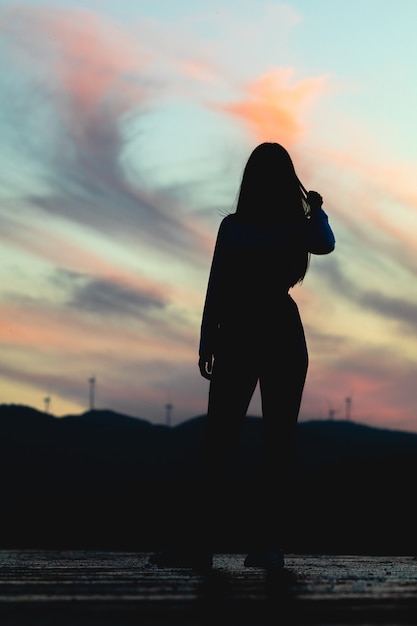 Silhouette d'une fille solitaire dans le champ posant au coucher du soleil