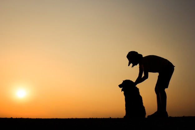 Silhouette de fille et son chien avec un beau fond de coucher de soleil.